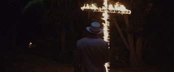 Movie still from “Live by Night” (2016), directed by Ben Affleck – A man wearing a white hat standing in front of a burning cross; Wide shot, High angle