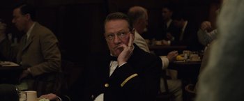 Movie still from “Live by Night” (2016), directed by Ben Affleck – A man in a suit and tie sitting in front of a group of people; Close Up shot, Over the shoulder angle