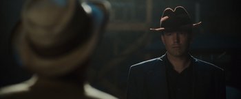 Movie still from “Live by Night” (2016), directed by Ben Affleck – A man wearing a suit and a hat is standing in front of a camera; Close Up shot, Over the shoulder angle