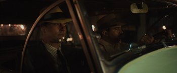 Movie still from “Live by Night” (2016), directed by Ben Affleck – A man in a suit and hat sitting in the back of a car; Close Up shot, Low angle