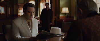 Movie still from “Live by Night” (2016), directed by Ben Affleck – A man sitting at a table in front of a cake; Medium shot, Over the shoulder angle