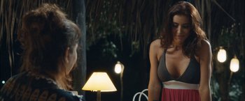 Movie still from “Liz in September” (2014), directed by Fina Torres – A woman standing next to a table with a lamp on top of it; Medium shot, Over the shoulder angle