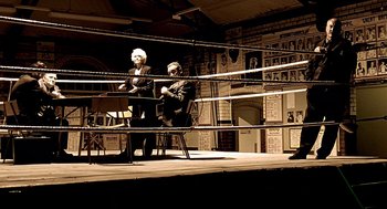 Movie still from “Lock, Stock and Two Smoking Barrels” (1998), directed by Guy Ritchie – Two people sitting in a boxing ring in front of each other; Wide shot, High angle