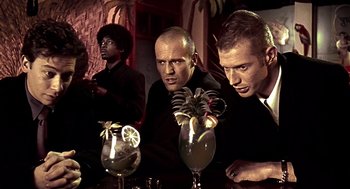 Movie still from “Lock, Stock and Two Smoking Barrels” (1998), directed by Guy Ritchie – A group of men sitting at a table with drinks; Medium shot, Low angle