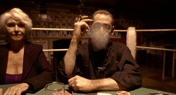 Movie still from “Lock, Stock and Two Smoking Barrels” (1998), directed by Guy Ritchie – A man sitting at a table smoking a cigarette; Medium shot, Low angle