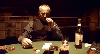 Movie still from “Lock, Stock and Two Smoking Barrels” (1998), directed by Guy Ritchie – An older man sitting at a table with cards and a glass; Medium shot, Low angle