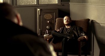 Movie still from “Lock, Stock and Two Smoking Barrels” (1998), directed by Guy Ritchie – A man sitting in a chair in front of an antique safe; Medium shot, Low angle