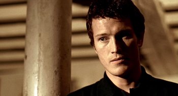 Movie still from “Lock, Stock and Two Smoking Barrels” (1998), directed by Guy Ritchie – A young man in a black shirt is looking at the camera; Close Up shot, Low angle
