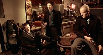 Movie still from “Lock, Stock and Two Smoking Barrels” (1998), directed by Guy Ritchie – Two men in suits and ties sitting in a room; Medium shot, Low angle