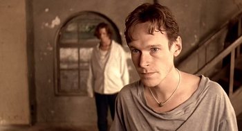 Movie still from “Lock, Stock and Two Smoking Barrels” (1998), directed by Guy Ritchie – A man standing next to another man in a room; Close Up shot, Over the shoulder angle