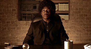 Movie still from “Lock, Stock and Two Smoking Barrels” (1998), directed by Guy Ritchie – A man sitting at a table in front of a brick wall; Close Up shot, Low angle