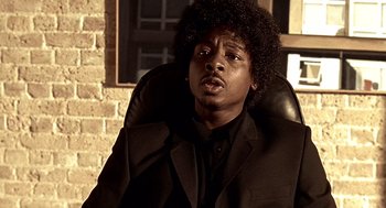 Movie still from “Lock, Stock and Two Smoking Barrels” (1998), directed by Guy Ritchie – A man sitting in a chair wearing a black suit; Close Up shot, Low angle