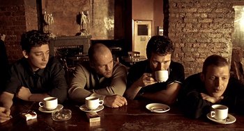 Movie still from “Lock, Stock and Two Smoking Barrels” (1998), directed by Guy Ritchie – A couple of men sitting at a table drinking coffee; Medium shot, Low angle