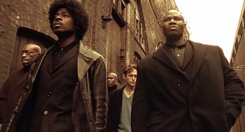 Movie still from “Lock, Stock and Two Smoking Barrels” (1998), directed by Guy Ritchie – A group of men standing next to each other on a street; Medium shot, Low angle