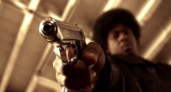Movie still from “Lock, Stock and Two Smoking Barrels” (1998), directed by Guy Ritchie – A man is holding a gun in his hand; Extreme Close Up shot, Low angle