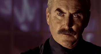 Movie still from “Lock, Stock and Two Smoking Barrels” (1998), directed by Guy Ritchie – An older man with a mustache and a goatee stares at the camera; Close Up shot, Low angle