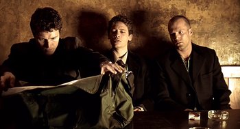 Movie still from “Lock, Stock and Two Smoking Barrels” (1998), directed by Guy Ritchie – A group of men sitting around a table holding a bag; Medium shot, Low angle