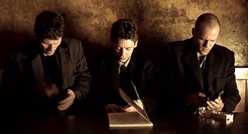 Movie still from “Lock, Stock and Two Smoking Barrels” (1998), directed by Guy Ritchie – A man sitting at a table writing in a notebook; Medium shot, Low angle