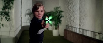 Movie still from “Logan's Run” (1976), directed by Michael Anderson – A young man holding a toy gun in a room with potted plants; Medium shot, Low angle