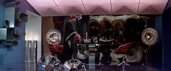 Movie still from “Logan's Run” (1976), directed by Michael Anderson – A woman standing in front of a mirror in a room; Wide shot, Over the shoulder angle