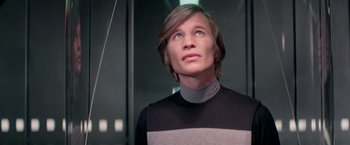 Movie still from “Logan's Run” (1976), directed by Michael Anderson – A man with long hair wearing a black and gray shirt; Close Up shot, Low angle