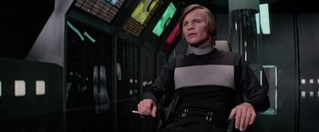 Movie still from “Logan's Run” (1976), directed by Michael Anderson – A man sitting in a chair in front of a window; Medium shot, Low angle