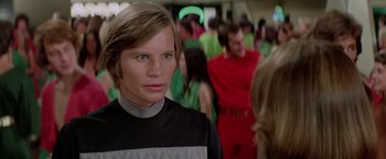 Movie still from “Logan's Run” (1976), directed by Michael Anderson – A man in a black and white shirt is in a crowd; Close Up shot, Low angle