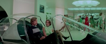 Movie still from “Logan's Run” (1976), directed by Michael Anderson – A man and a woman sitting in a chair; Wide shot, High angle