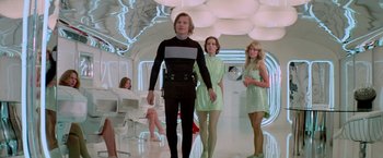 Movie still from “Logan's Run” (1976), directed by Michael Anderson – A group of women in a room with a man in a black suit; Wide shot, Low angle