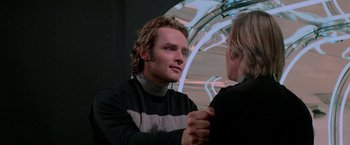 Movie still from “Logan's Run” (1976), directed by Michael Anderson – A man in a black and white sweater talking to another man in a black and white sweater; Close Up shot, Over the shoulder angle