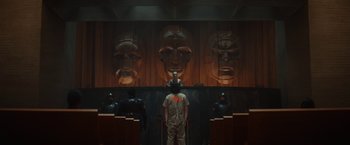 Movie still from “Loki” (2021), created by Michael Waldron – A man standing in front of a wall with faces on it; Wide shot, Low angle