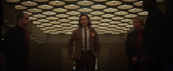 Movie still from “Loki” (2021), created by Michael Waldron – A man in a suit and tie standing in front of a ceiling; Medium shot, Low angle