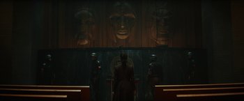 Movie still from “Loki” (2021), created by Michael Waldron – A group of men standing in front of a wall with faces on it; Wide shot, Low angle