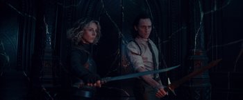A woman and a man holding swords in a dark room