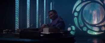 Movie still from “Loki” (2021), created by Michael Waldron – A man sitting in front of a stack of books; Medium shot, Over the shoulder angle