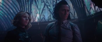 Movie still from “Loki” (2021), created by Michael Waldron – A man with long black hair standing next to a woman; Medium shot, Over the shoulder angle