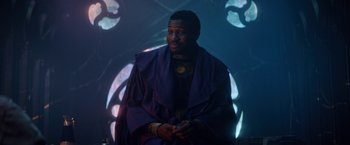 Movie still from “Loki” (2021), created by Michael Waldron – A man wearing a purple robe sitting on a chair; Medium shot, Low angle