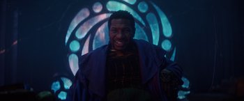 Movie still from “Loki” (2021), created by Michael Waldron – A man smiling in front of a stained - glass window; Medium shot, Low angle