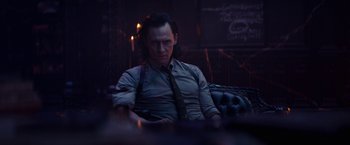 Movie still from “Loki” (2021), created by Michael Waldron – A man sitting on a couch in a dark room; Medium shot, Over the shoulder angle