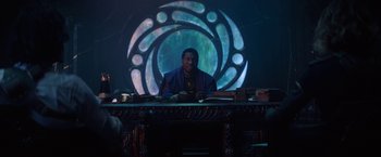 Movie still from “Loki” (2021), created by Michael Waldron – A man sitting at a table in front of a projection of a circle; Medium shot, Over the shoulder angle