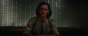 Movie still from “Loki” (2021), created by Michael Waldron – A man with long black hair sitting in front of a metal wall; Medium shot, Over the shoulder angle
