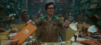 Movie still from “Loki” (2021), created by Michael Waldron – A man in a brown and green jacket is standing in front of a table; Medium shot, Low angle