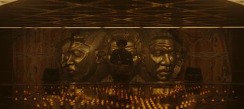 Movie still from “Loki” (2021), created by Michael Waldron – A man standing in front of a wall with faces on it; Extreme Wide shot, Overhead angle