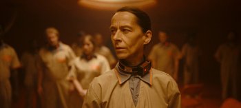 Movie still from “Loki” (2021), created by Michael Waldron – A man with a collar around his neck is standing in front of a group of people; Close Up shot, Low angle
