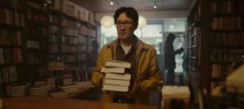 Movie still from “Loki” (2021), created by Michael Waldron – A man holding a stack of books in a bookstore; Medium shot, Low angle