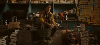 Movie still from “Loki” (2021), created by Michael Waldron – A man sitting on top of a chair next to a microphone; Medium shot, High angle