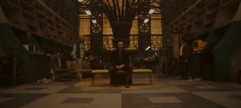 Movie still from “Loki” (2021), created by Michael Waldron – A man sitting on top of a yellow bench in a room; Wide shot, Low angle