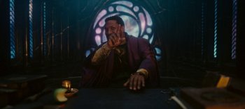 Movie still from “Loki” (2021), created by Michael Waldron – A man sitting at a table in front of a stained glass window; Medium shot, Over the shoulder angle