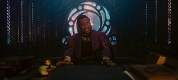 Movie still from “Loki” (2021), created by Michael Waldron – A man sitting at a table in front of a stained glass window; Medium shot, Over the shoulder angle