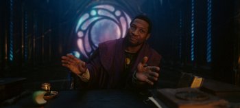Movie still from “Loki” (2021), created by Michael Waldron – A man in a purple robe sitting in front of a table; Medium shot, Low angle